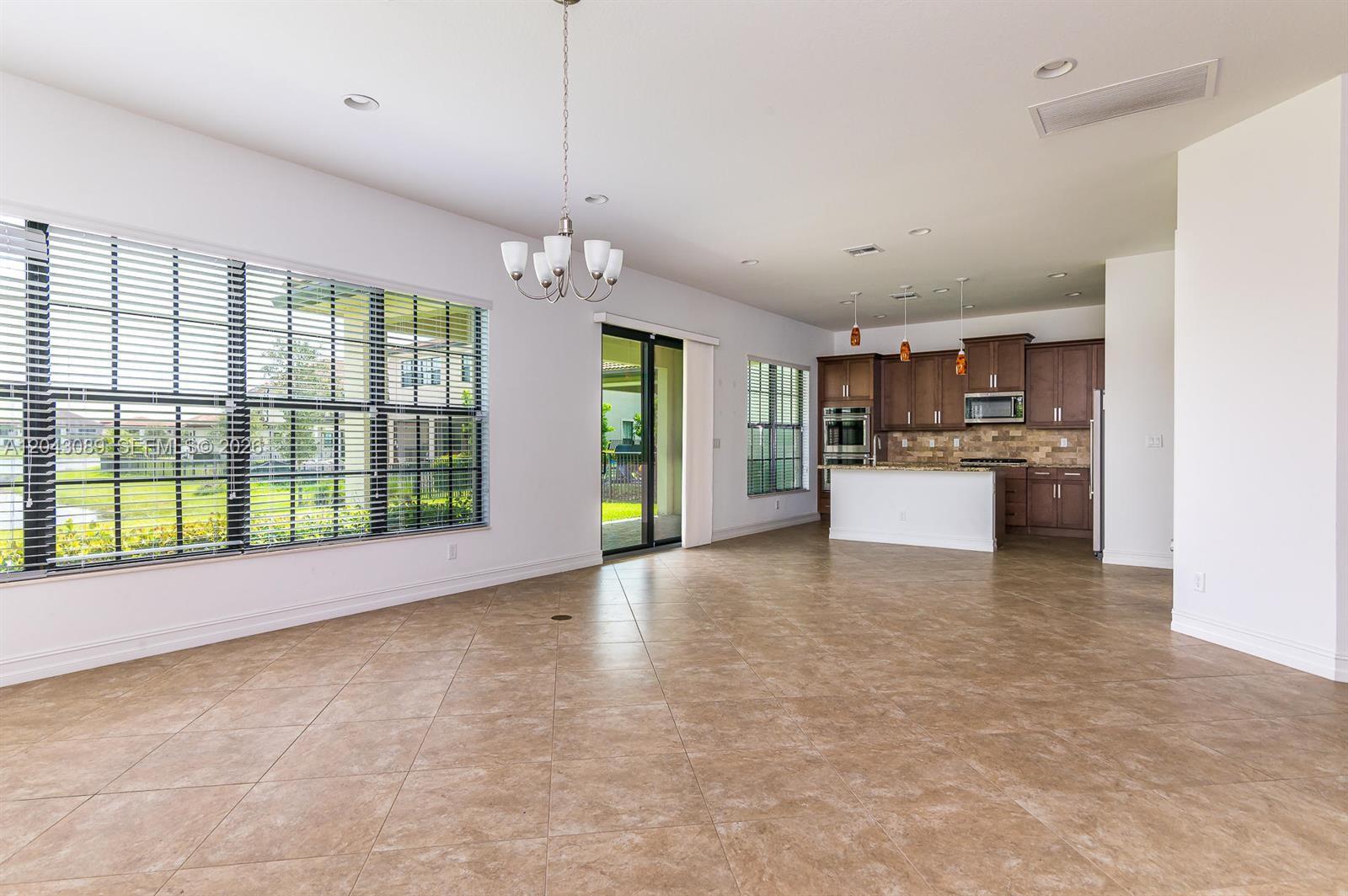 An open-concept kitchen and dining area features tile flooring, dark wood cabinetry, and large windows — 9350 Solstice Cir, Parkland FL 33076, PARKLAND, FL