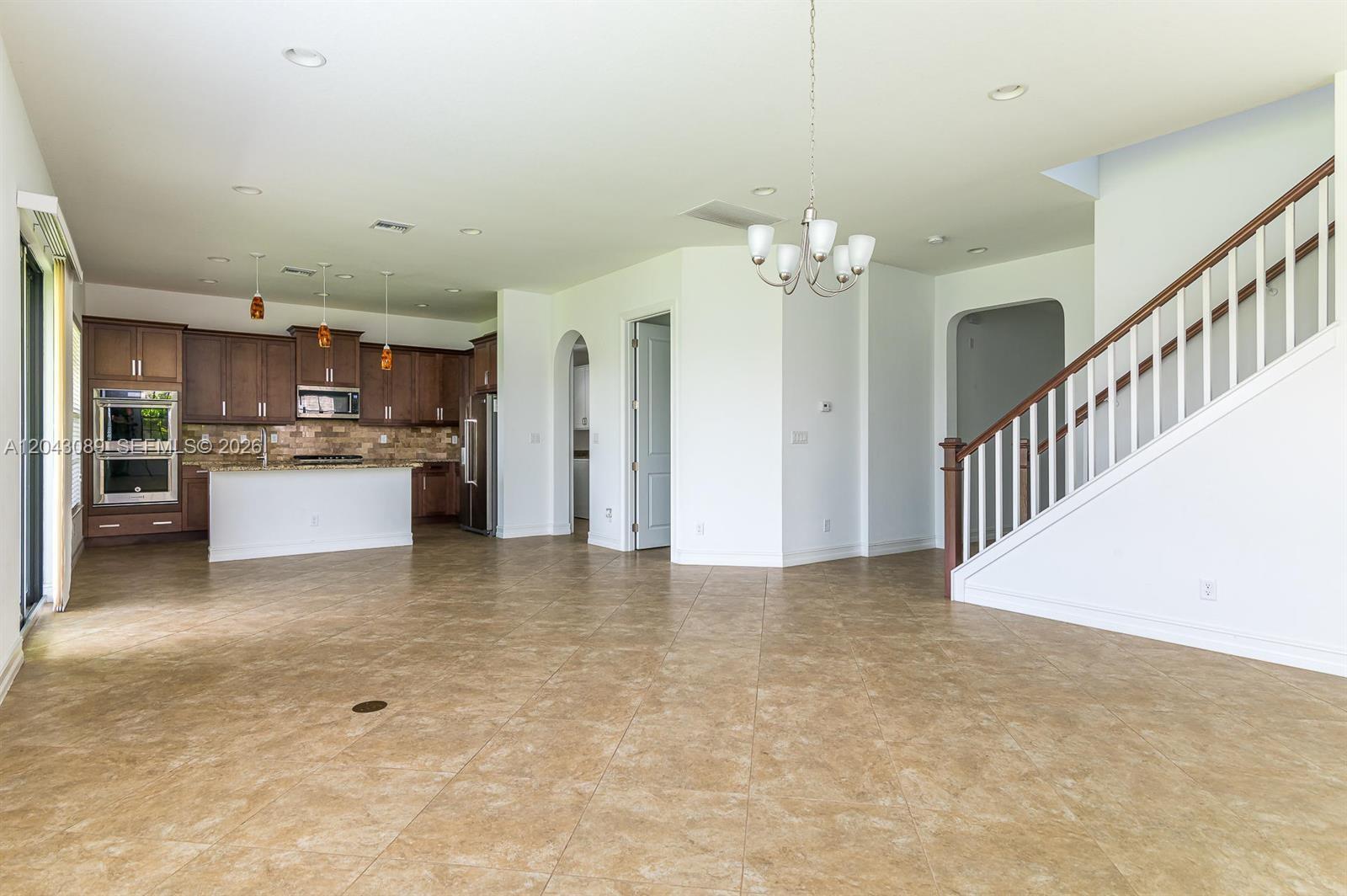 An open-concept kitchen and living area features tile flooring, dark wood cabinetry, and a staircase — 9350 Solstice Cir, Parkland FL 33076, PARKLAND, FL