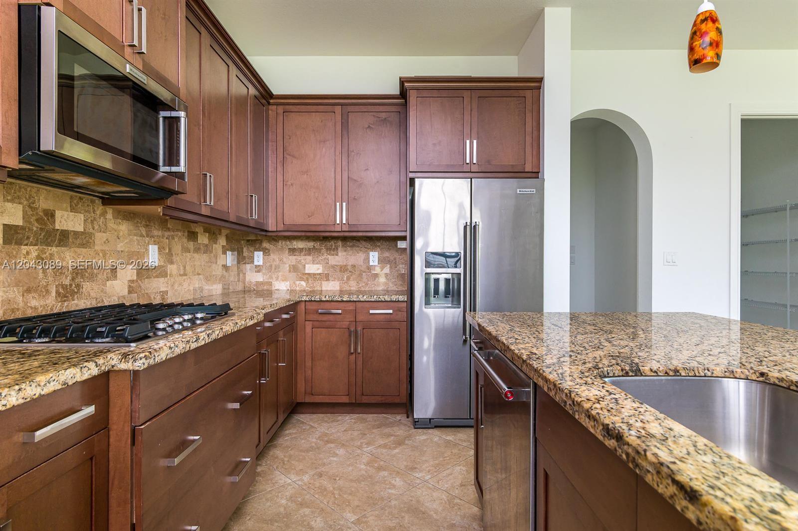 A kitchen features dark wood cabinets, granite countertops, stainless steel appliances, and a tiled backsplash — 9350 Solstice Cir, Parkland FL 33076, PARKLAND, FL