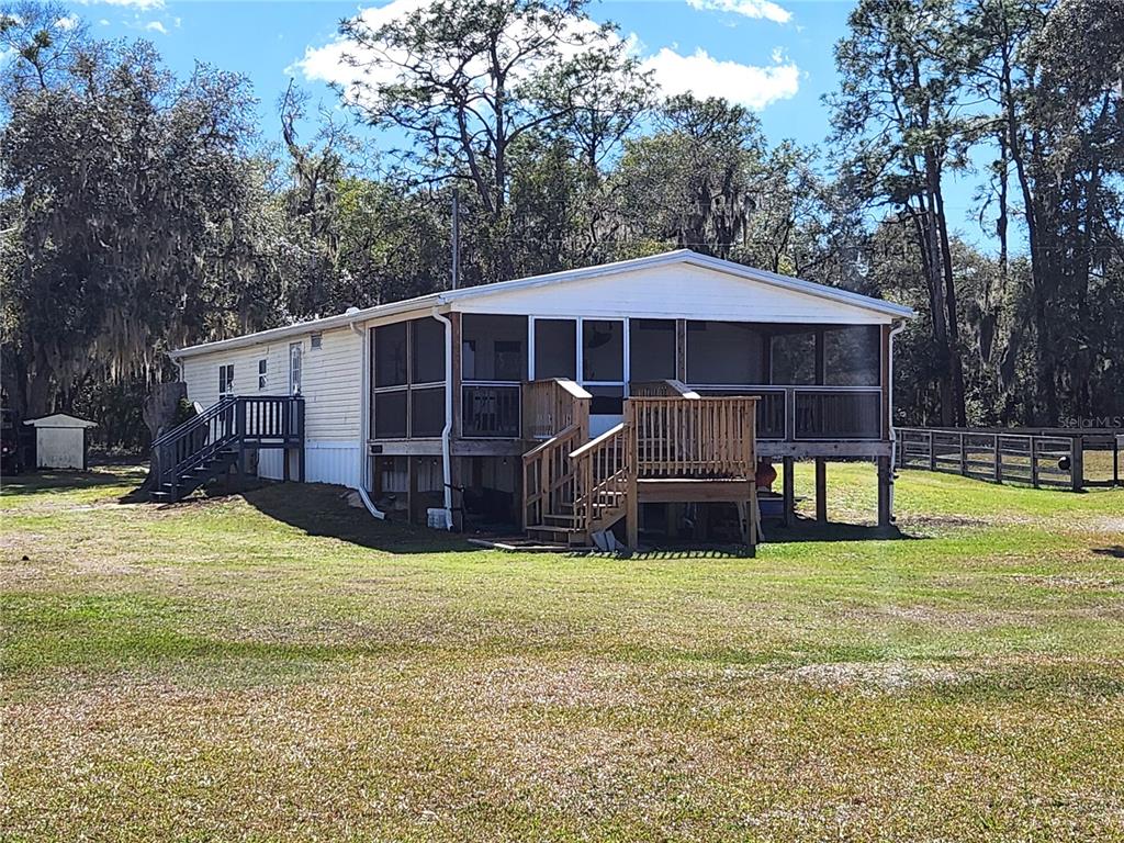 A single-story manufactured home with a screened-in porch and wooden deck sits on a grassy lot — 10915 NE 222ND STREET, FORT MC COY, FL