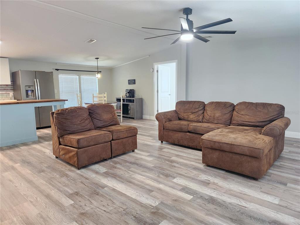 A living room with wood-look flooring, a brown sectional, a loveseat, and an open kitchen — 10915 NE 222ND STREET, FORT MC COY, FL