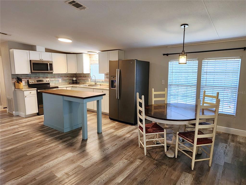 A kitchen features white cabinets, a blue island, stainless steel appliances, and wood-look flooring — 10915 NE 222ND STREET, FORT MC COY, FL