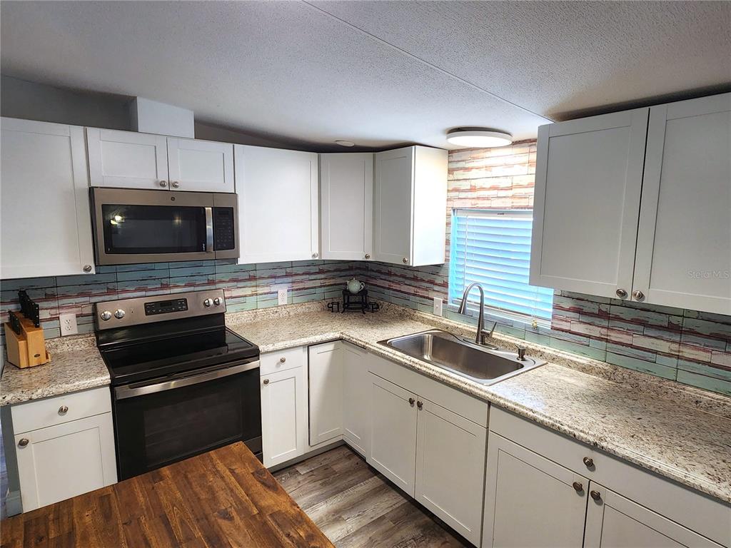 A kitchen features white cabinets, granite countertops, a stainless steel microwave, and a tiled backsplash — 10915 NE 222ND STREET, FORT MC COY, FL
