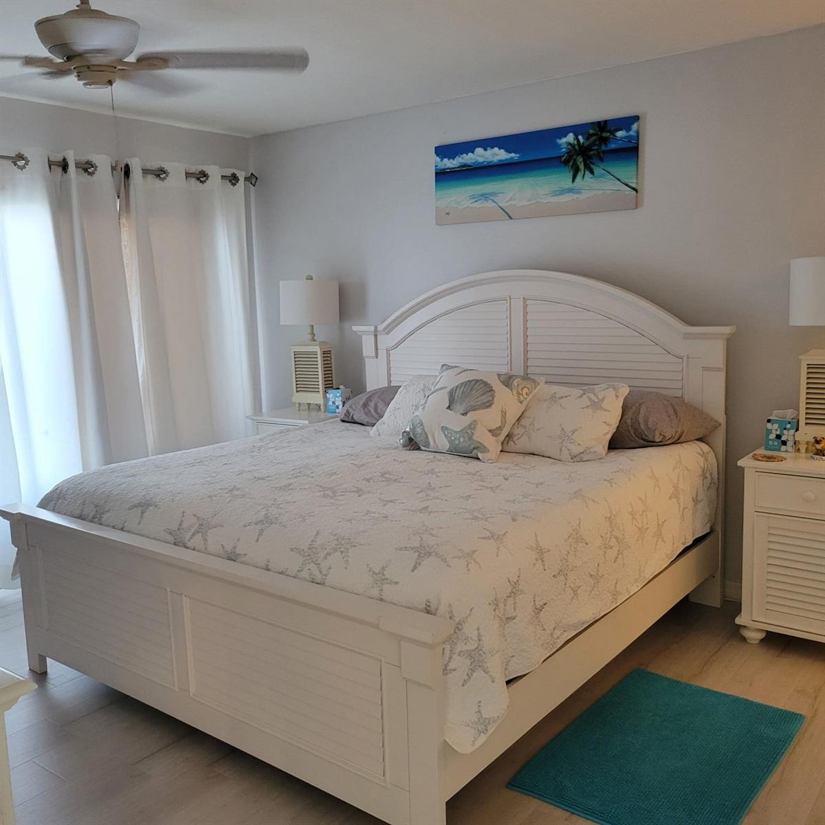 A bedroom features a white bed frame, coastal-themed bedding, and a beach-scene wall art piece — 10310 S Ocean Drive # 507, Jensen Beach FL 34957, JENSEN BEACH, FL