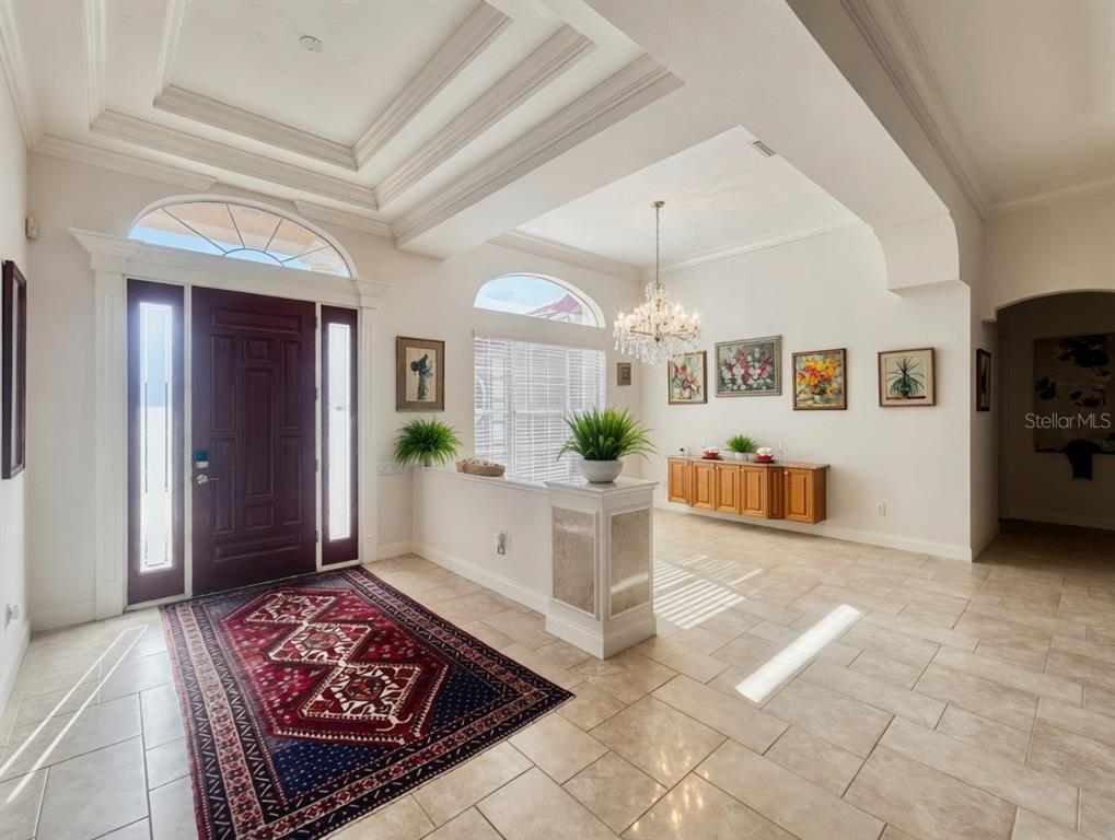 A bright foyer features a dark wood front door, tile flooring, and a crystal chandelier — 9110 DEER COURT, VENICE, FL