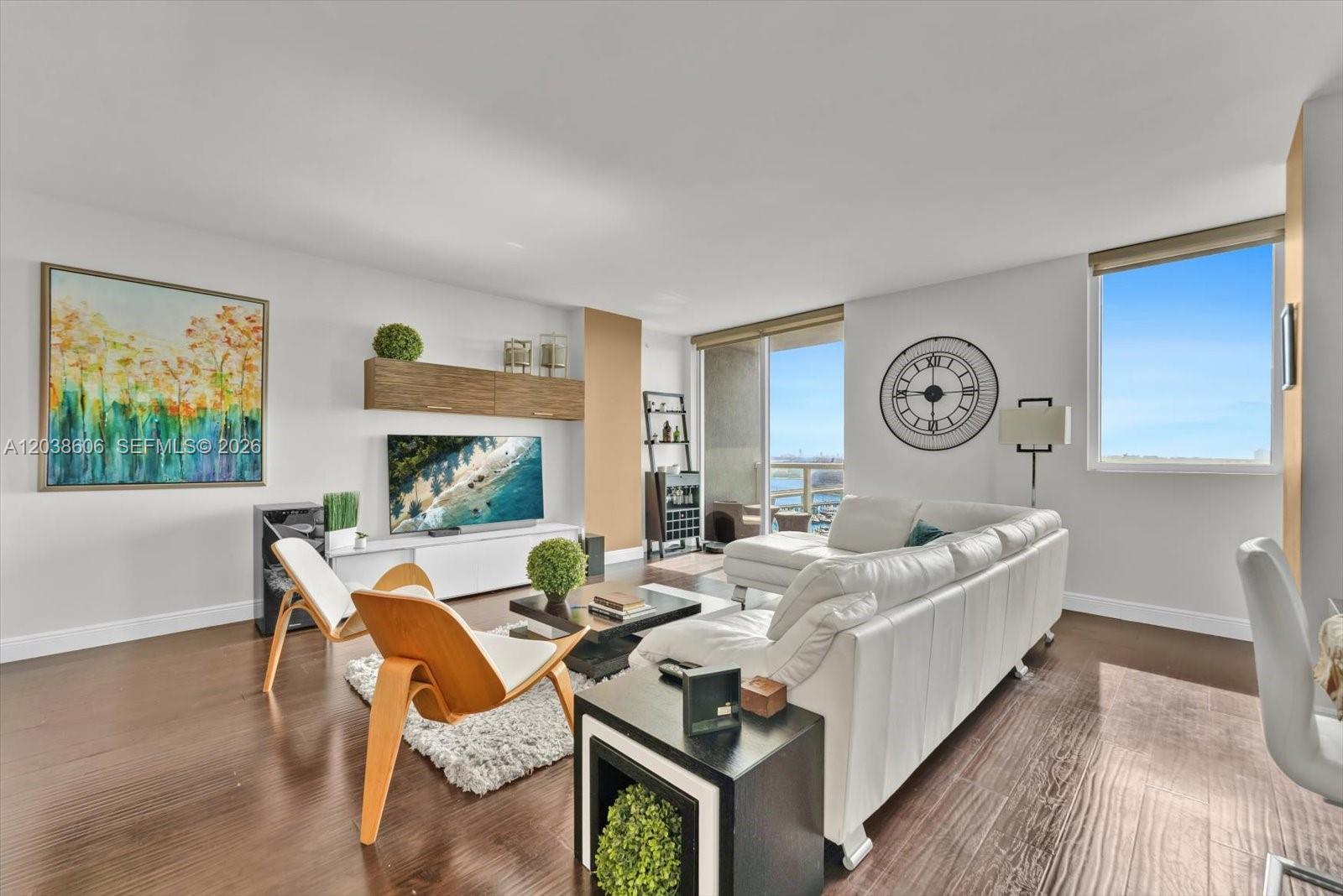 A modern living room features a white sectional sofa, wood-accented furniture, and a large wall clock — 244 Biscayne Blvd # 1803, Miami FL 33132, MIAMI, FL