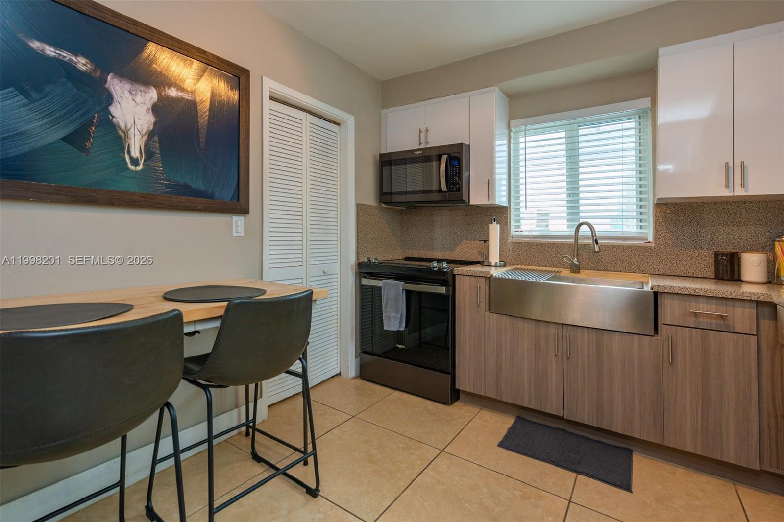 A kitchen features a stainless steel farmhouse sink, wood-tone cabinets, and a small dining area — 2925 NW 11th Ave, Miami FL 33127, MIAMI, FL