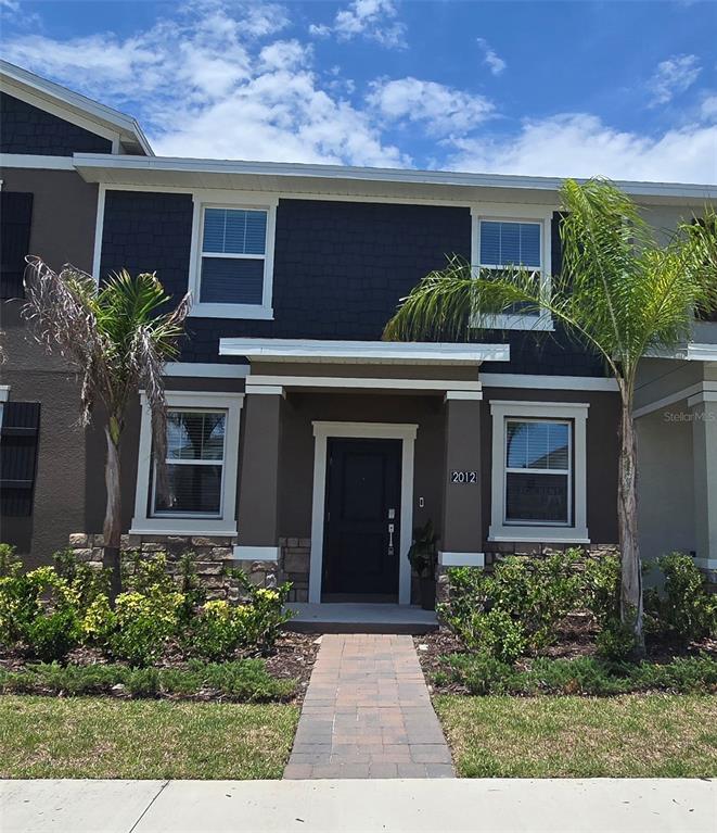 A two-story townhouse exterior features dark siding, stone accents, and a paved walkway — 2012 TOHOQUA BOULEVARD, KISSIMMEE, FL