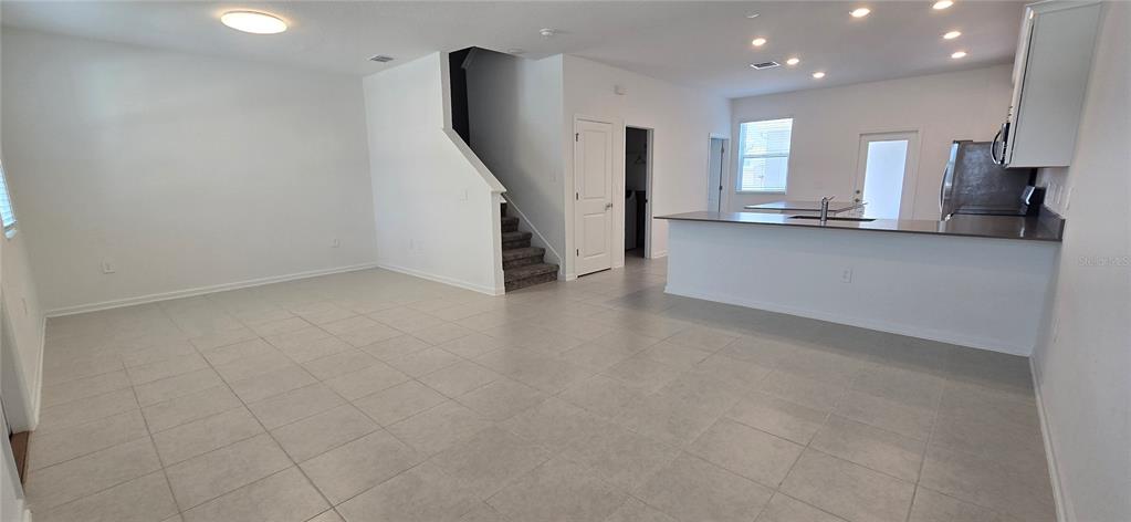 An open-concept living area features light tile flooring, a kitchen island, and a staircase — 2012 TOHOQUA BOULEVARD, KISSIMMEE, FL