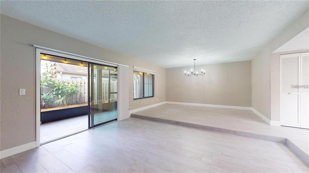 A living area with light tile flooring features a sunken dining space and sliding glass doors — 202 PINE CONE TRAIL, ORMOND BEACH, FL