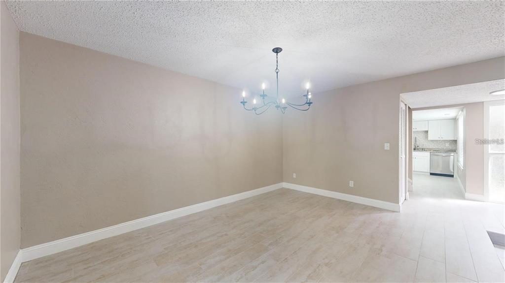 An empty dining room features light-colored tile flooring, beige walls, and a black chandelier — 202 PINE CONE TRAIL, ORMOND BEACH, FL