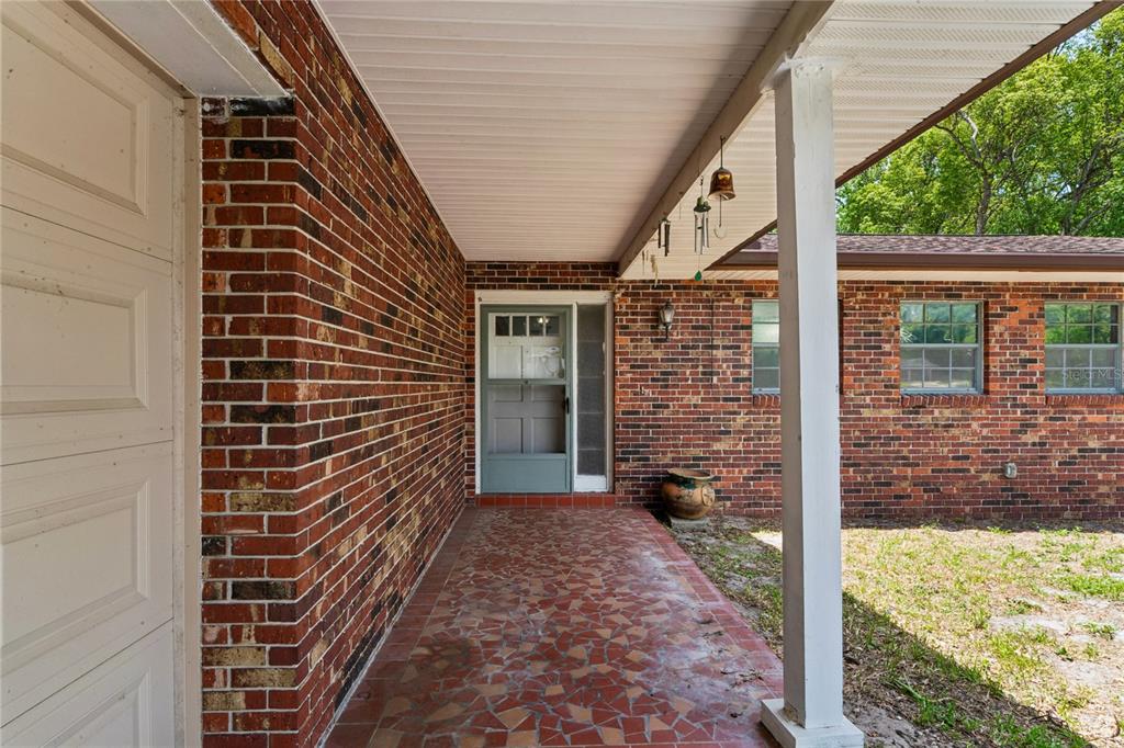 A covered brick porch features a tiled floor, a white support column, and a door — 1022 S MILDRED AVENUE, BROOKSVILLE, FL