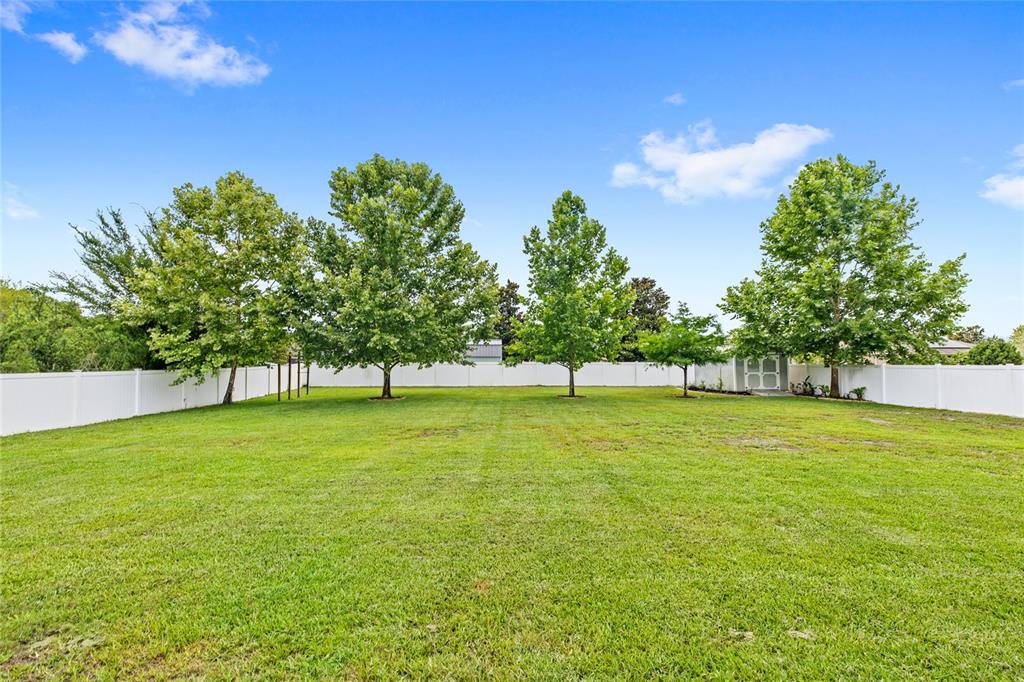 A large, grassy backyard features several mature trees and a white vinyl privacy fence — 122 LOS ARBOR DRIVE, DELAND, FL
