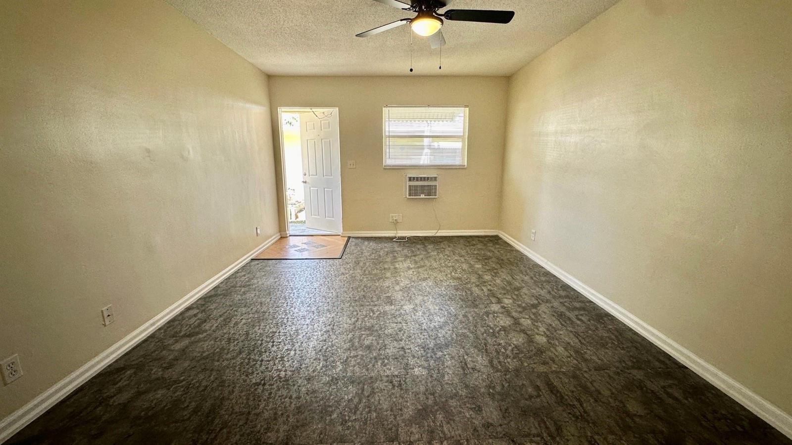 An empty room features beige walls, a ceiling fan, a window air conditioner, and dark flooring — 1973 #1 NE 4th Street, Deerfield Beach FL 33441, DEERFIELD BEACH, FL