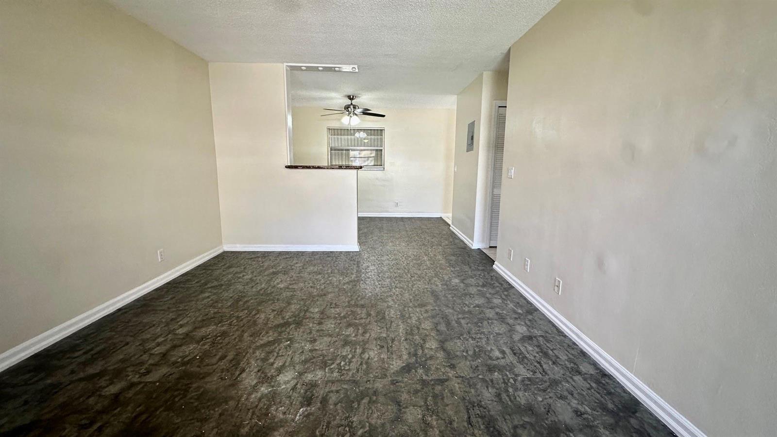 An empty room features dark gray flooring, beige walls, and a pass-through to the kitchen — 1973 #1 NE 4th Street, Deerfield Beach FL 33441, DEERFIELD BEACH, FL