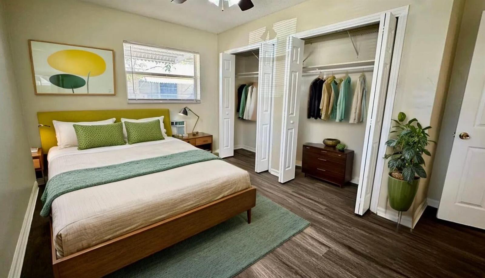 A bedroom features a bed with a green headboard, wood flooring, and two open closets — 1973 #1 NE 4th Street, Deerfield Beach FL 33441, DEERFIELD BEACH, FL