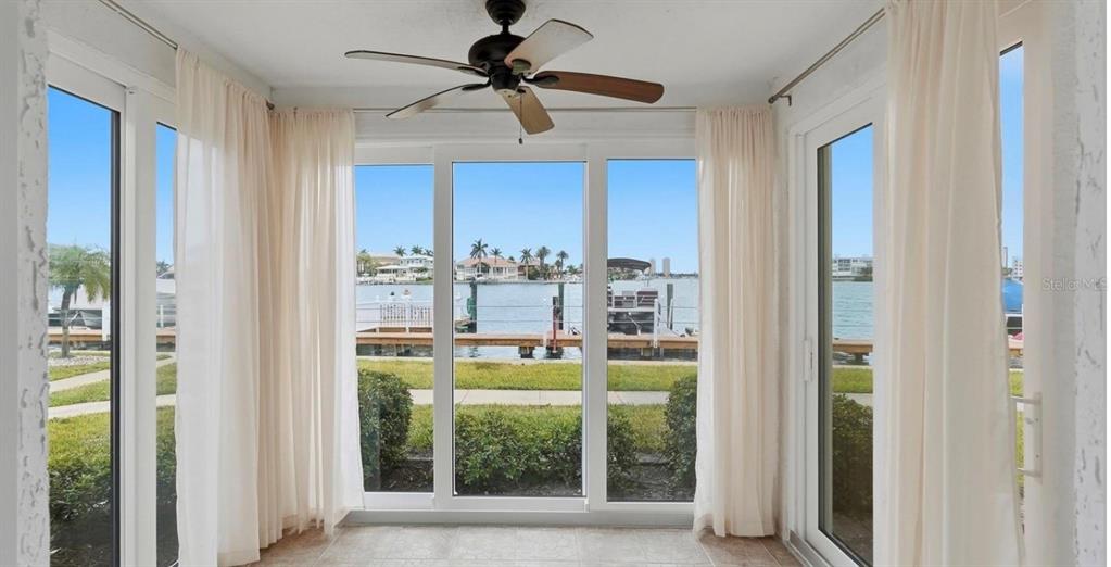 A sunroom with a ceiling fan, tile floors, and large windows overlooking a waterfront dock — 8921 BLIND PASS ROAD UNIT 144, ST PETE BEACH, FL