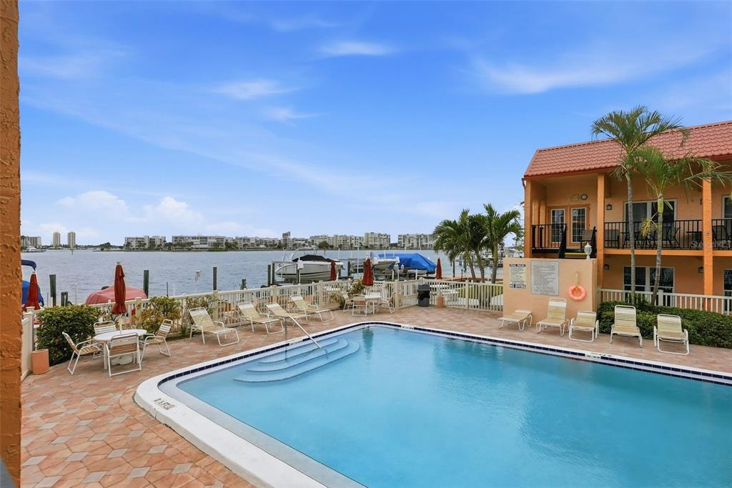 A swimming pool sits on a patio overlooking a bay with boats and distant buildings — 8921 BLIND PASS ROAD UNIT 144, ST PETE BEACH, FL