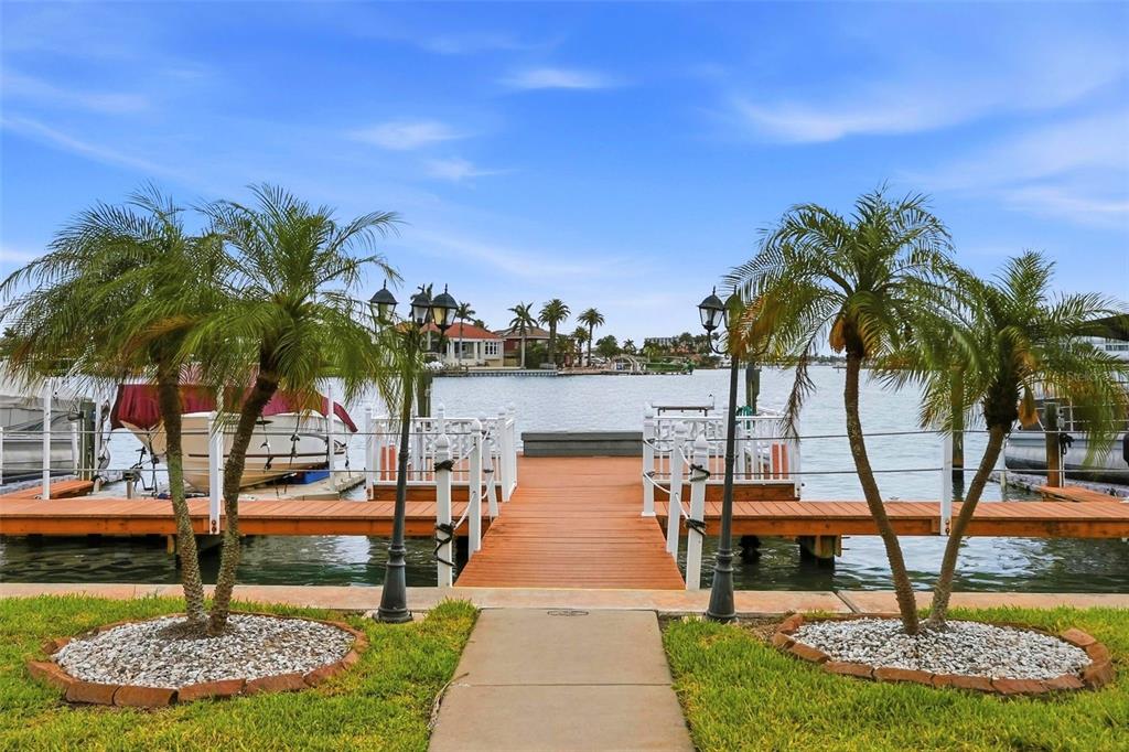 A wooden dock with two palm trees extends into a canal with boats docked nearby — 8921 BLIND PASS ROAD UNIT 144, ST PETE BEACH, FL