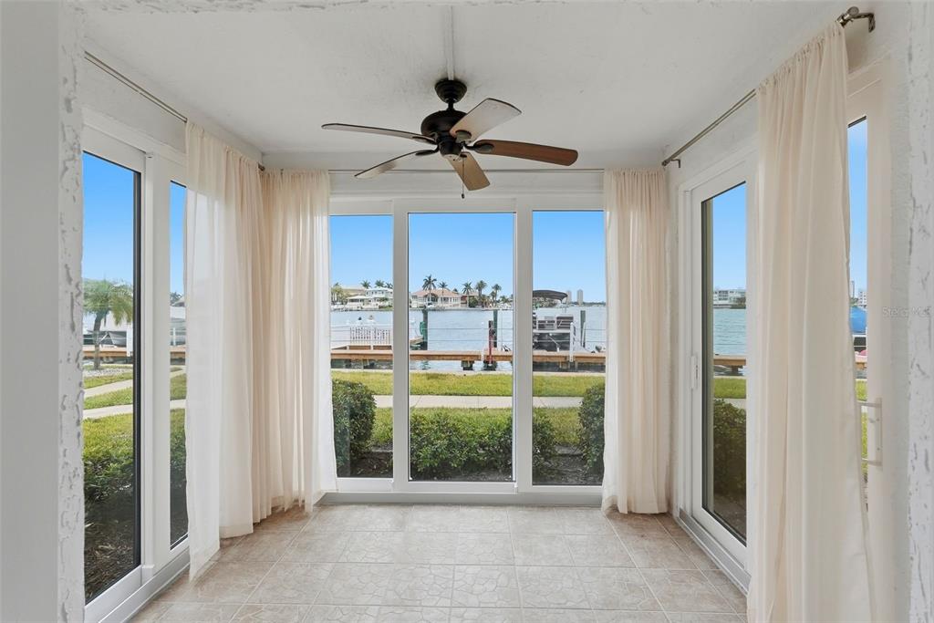 A sunroom with tile flooring, a ceiling fan, and large windows overlooking a waterfront dock — 8921 BLIND PASS ROAD UNIT 144, ST PETE BEACH, FL