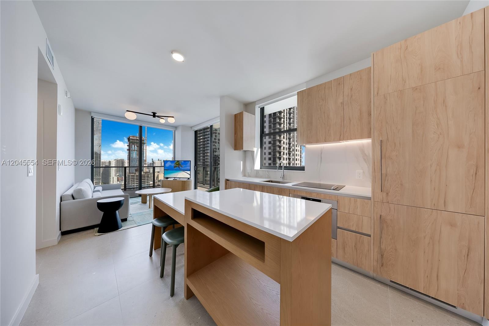 A modern kitchen with light wood cabinetry and a white island overlooks a living area — 11 NE 6th St # 3209, Miami FL 33132, MIAMI, FL
