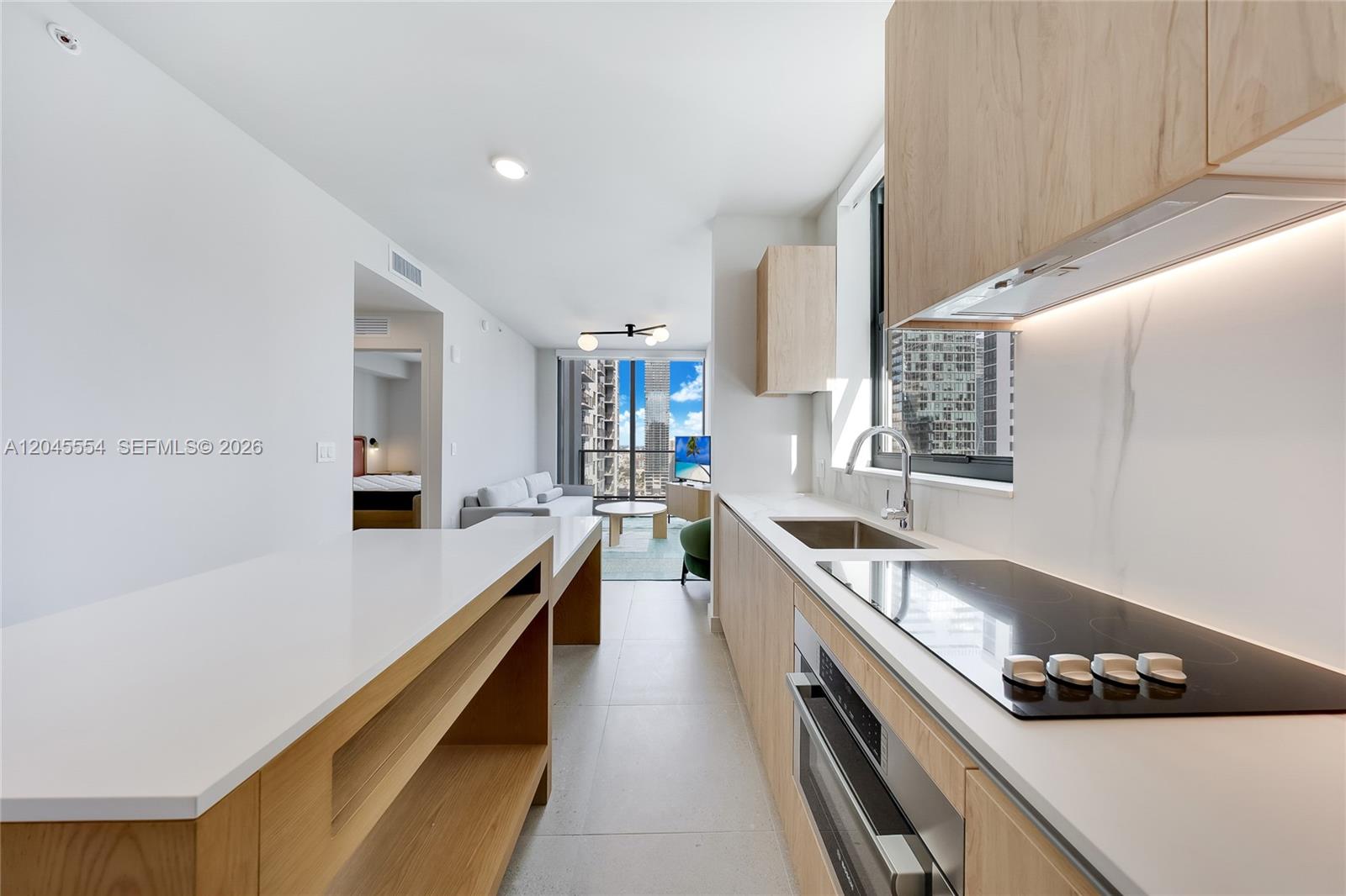 A modern kitchen with light wood cabinetry and white countertops overlooks a living area — 11 NE 6th St # 3209, Miami FL 33132, MIAMI, FL