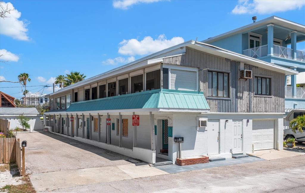 A two-story building with a teal metal awning, wood siding, and a gravel parking area — 40 77TH AVENUE, TREASURE ISLAND, FL