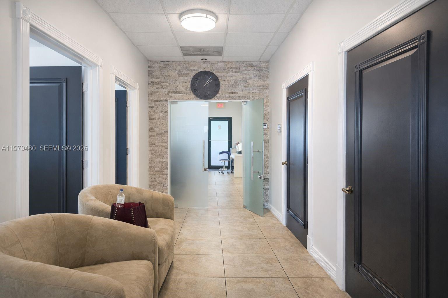 A hallway features beige tile floors, dark doors, and a stone accent wall with a clock — 2475 NW 95th Ave # 2, Doral FL 33172, DORAL, FL