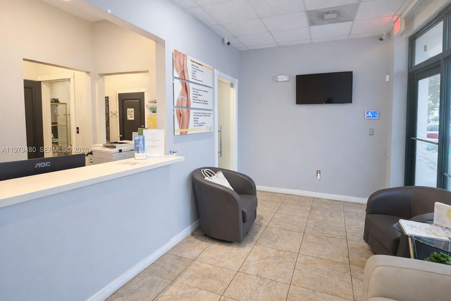 A waiting room features a reception desk, two armchairs, a television, and tiled flooring — 2475 NW 95th Ave # 2, Doral FL 33172, DORAL, FL