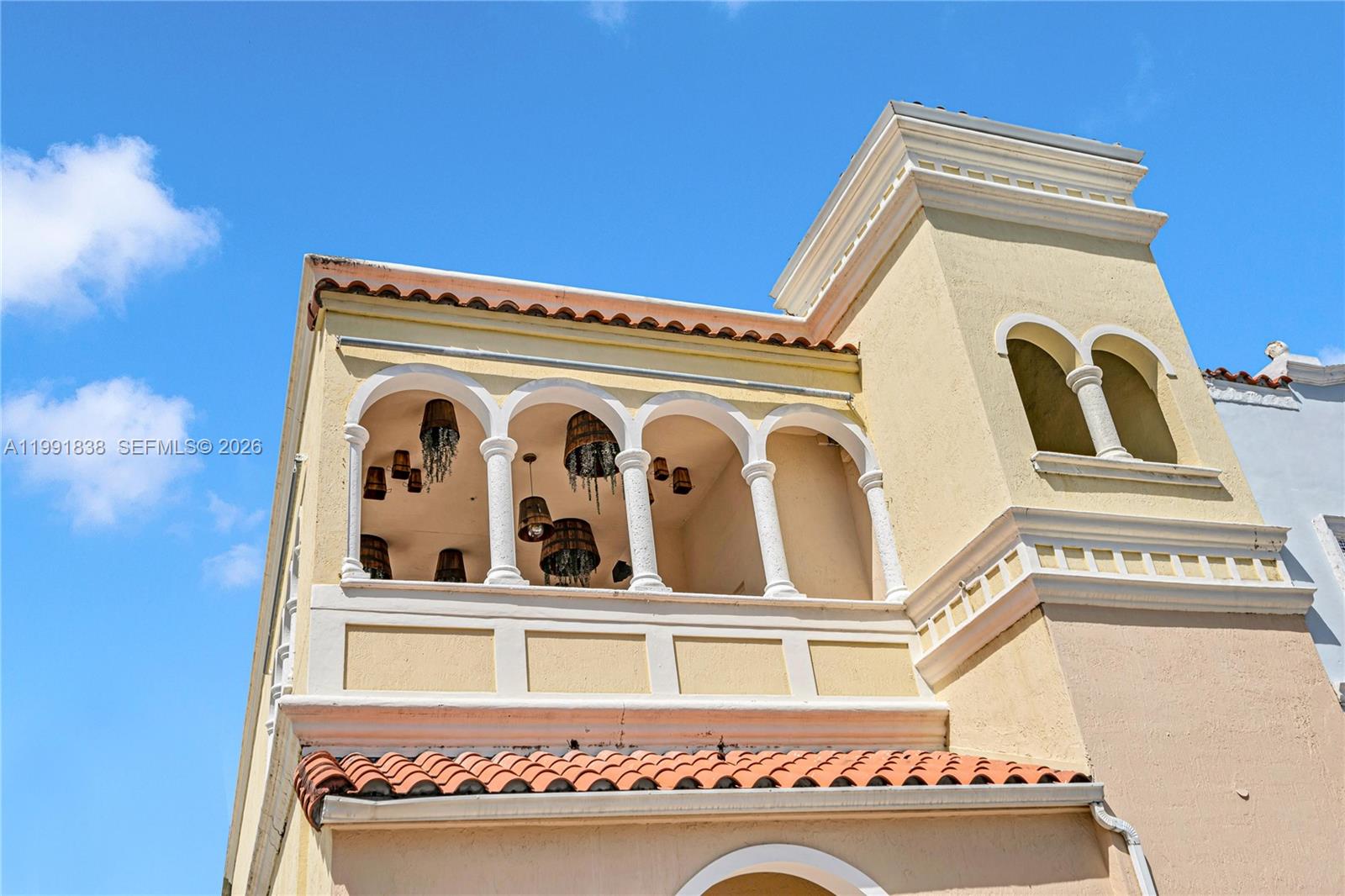 A yellow stucco building features an arched balcony with hanging basket-style light fixtures — 223 Valencia Ave, Coral Gables FL 33134, CORAL GABLES, FL