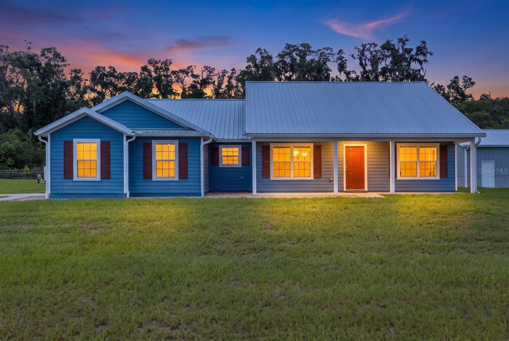 A blue single-story house with a metal roof and a red front door at dusk — 249 SW PLEASANT HILL GLEN, FORT WHITE, FL