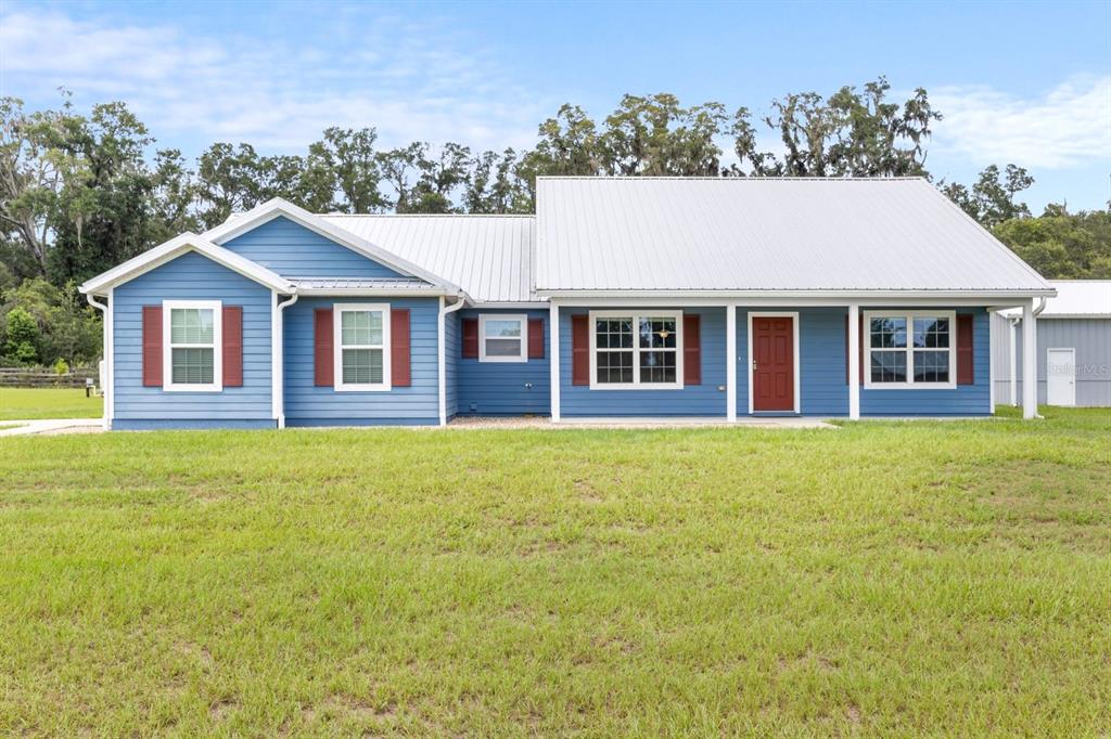 A blue single-story house with a white metal roof and red shutters sits on grass — 249 SW PLEASANT HILL GLEN, FORT WHITE, FL