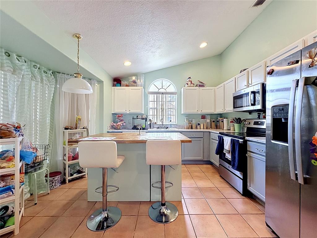 A kitchen features a central island with bar stools, white cabinets, and stainless steel appliances — 230 HYPOLITA AVENUE, DAVENPORT, FL