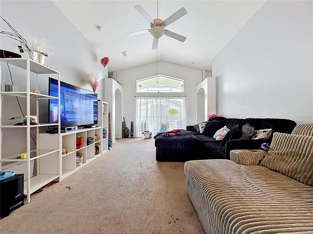 A living room features a vaulted ceiling, beige carpeting, a large television, and sectional seating — 230 HYPOLITA AVENUE, DAVENPORT, FL