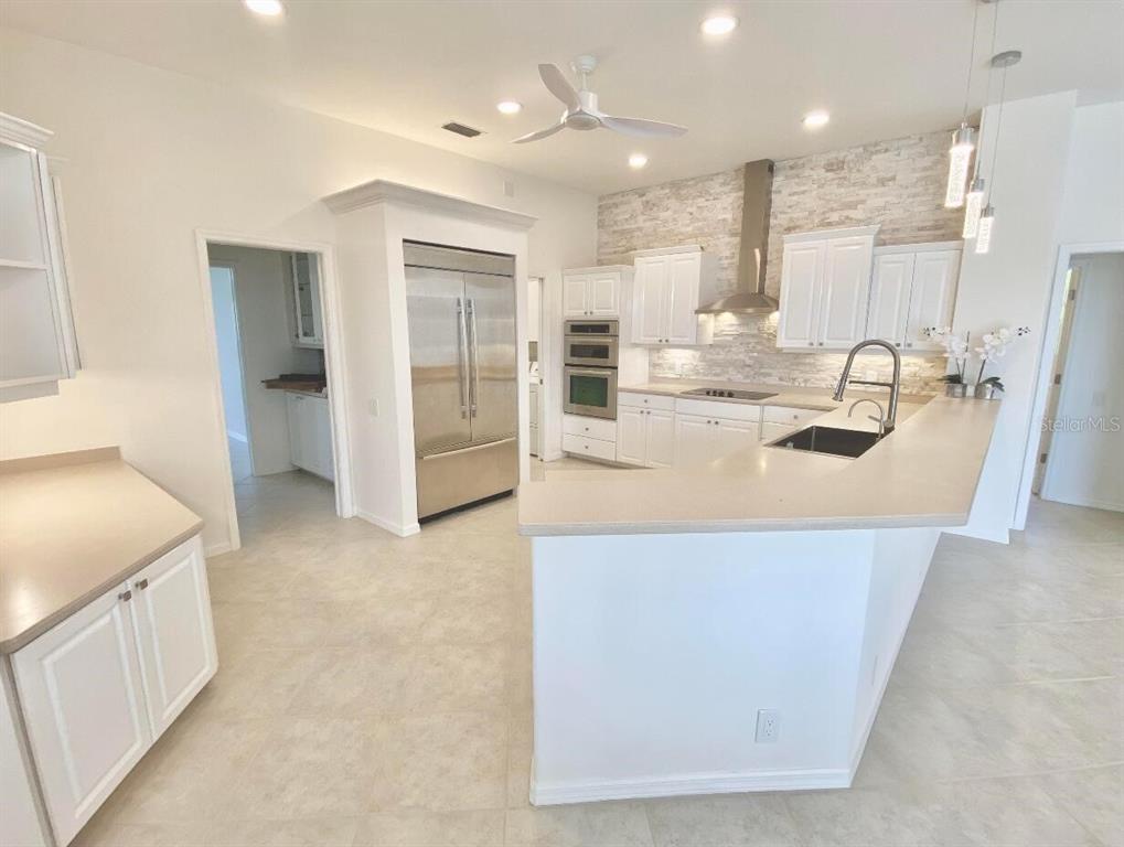 A bright kitchen features white cabinets, stainless steel appliances, and a large peninsula countertop — 7468 ROXYE LANE, SARASOTA, FL