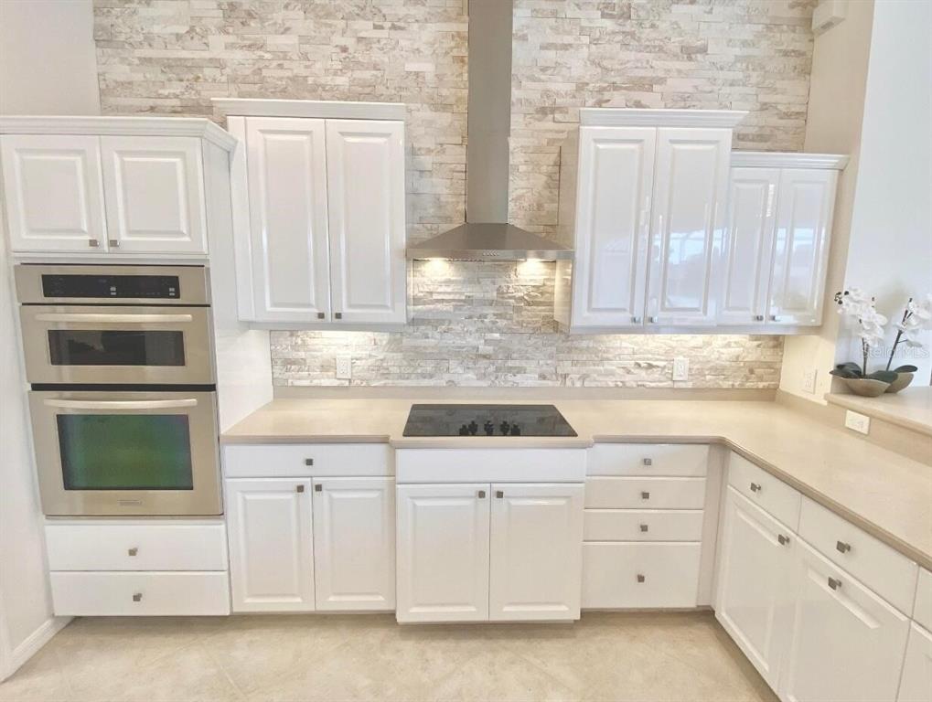 A kitchen features white cabinets, stainless steel appliances, a stone backsplash, and a cooktop — 7468 ROXYE LANE, SARASOTA, FL