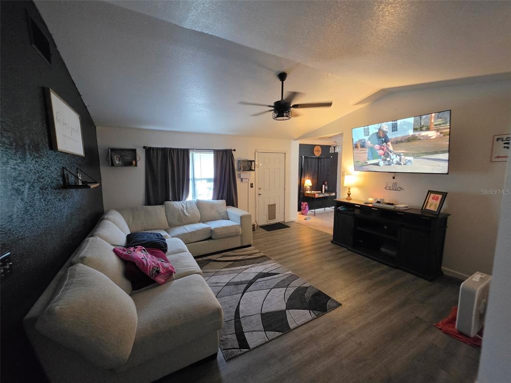 A living room features a sectional sofa, a wall-mounted television, and wood-look flooring — 720 SE PINE AVENUE, FORT MEADE, FL