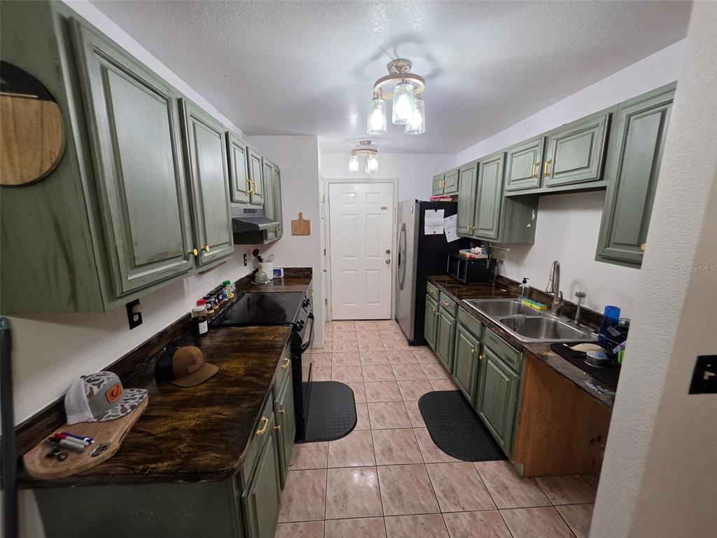 A kitchen features green cabinets, dark countertops, tile flooring, and stainless steel appliances — 720 SE PINE AVENUE, FORT MEADE, FL