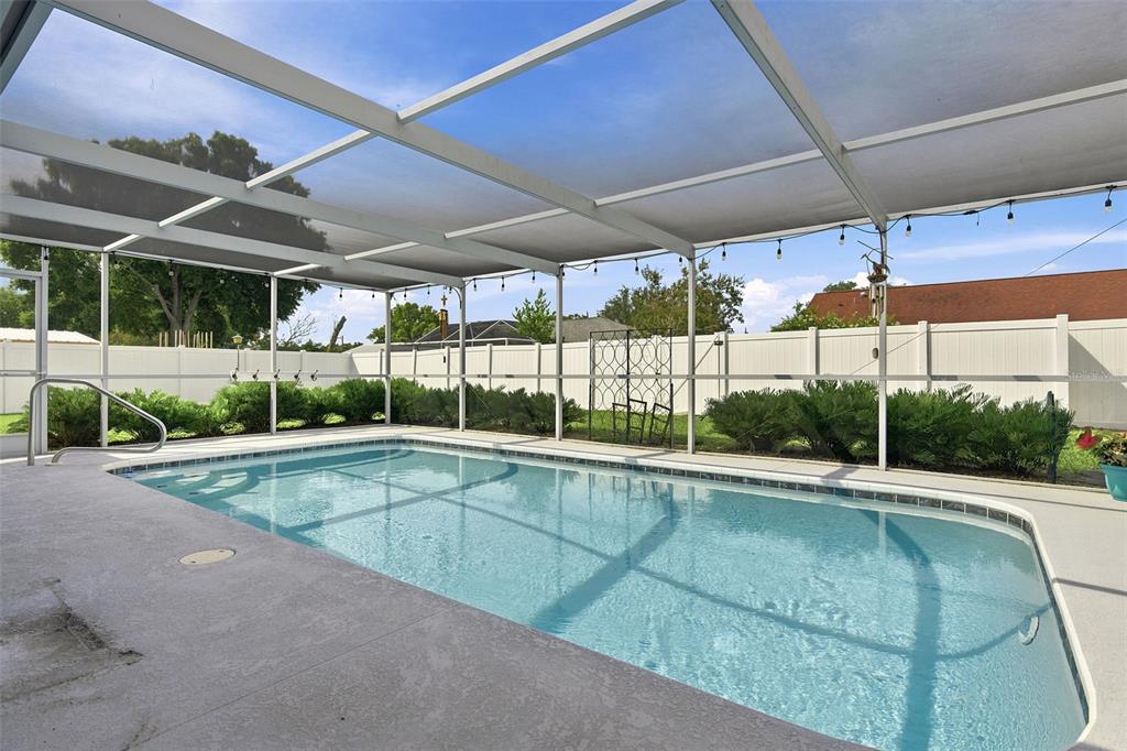 A rectangular swimming pool is enclosed by a screened lanai with a white vinyl fence — 4219 AUGUSTINE ROAD, SPRING HILL, FL