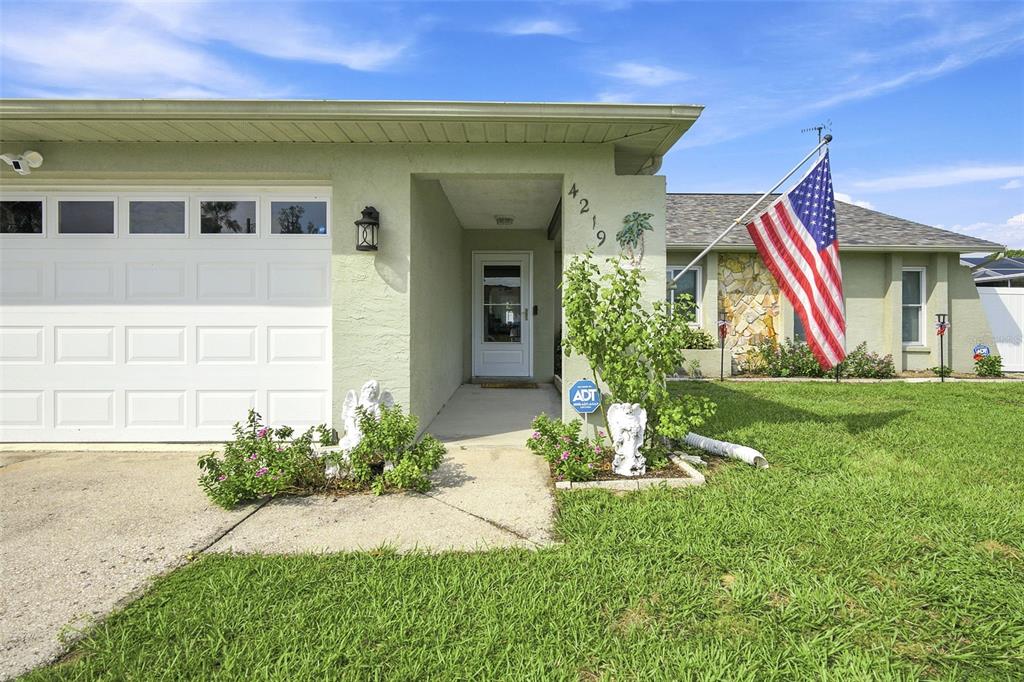 A single-story house with a light green exterior, a white garage door, and an American flag — 4219 AUGUSTINE ROAD, SPRING HILL, FL