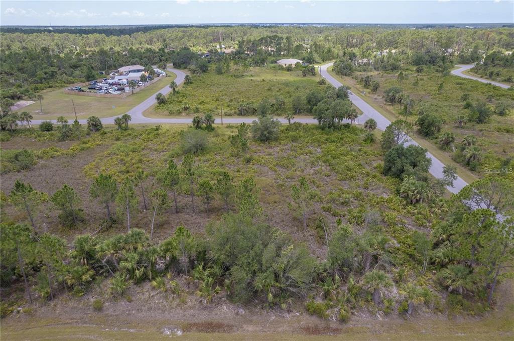 An aerial view shows a vacant, wooded lot bordered by paved roads and nearby houses — 218 GASTIN STREET, PORT CHARLOTTE, FL