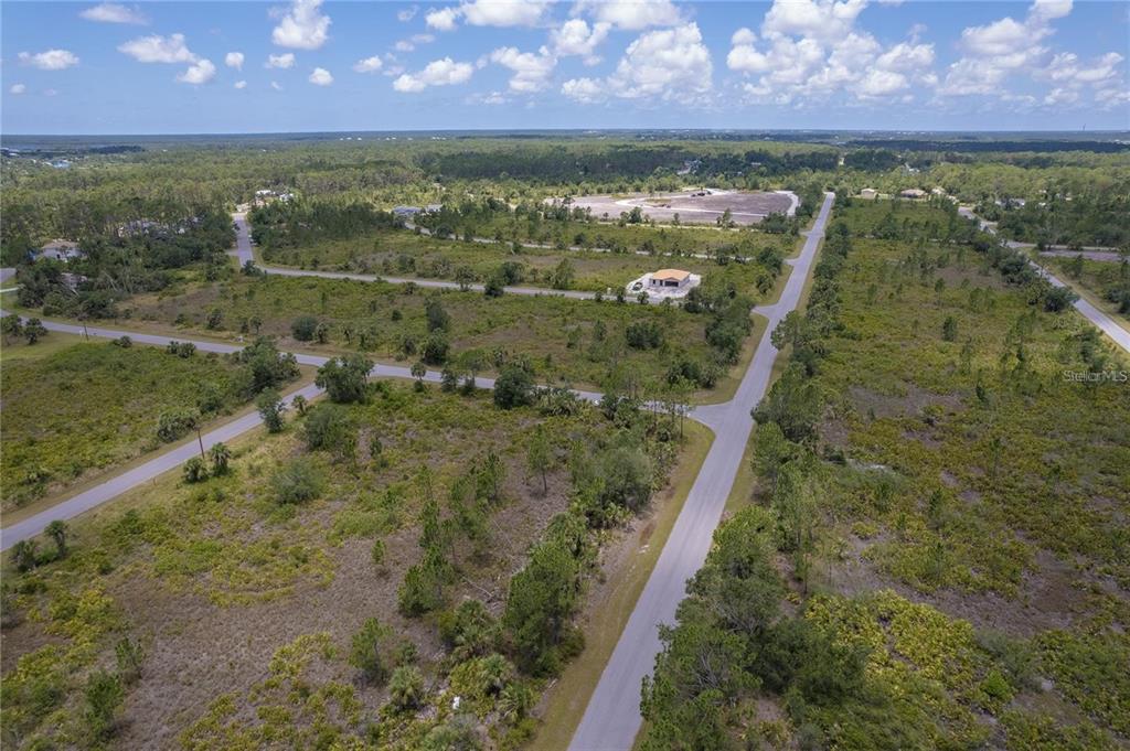 An aerial view shows a paved road intersecting through a large, undeveloped, grassy vacant lot — 218 GASTIN STREET, PORT CHARLOTTE, FL