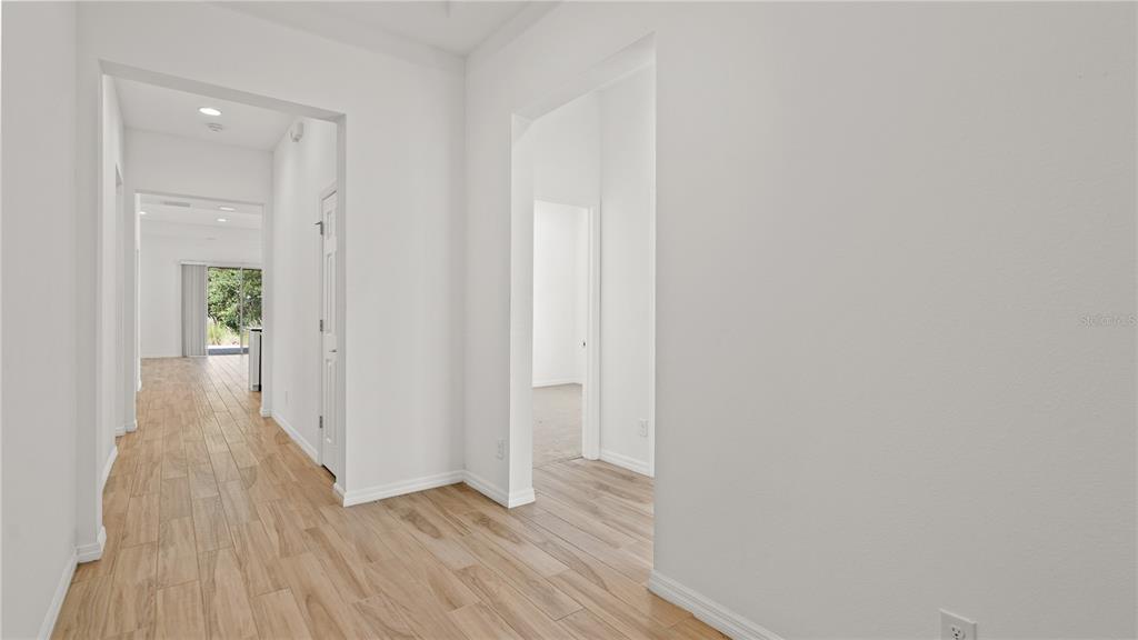A hallway with light wood-look tile flooring leads toward an open living area — 7964 HANSON BAY PLACE, KISSIMMEE, FL