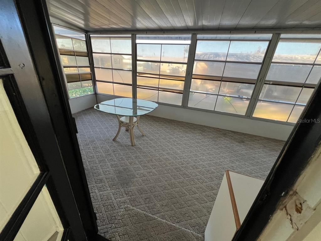 A sunroom features a glass-topped table, carpeted flooring, and large windows overlooking a neighborhood — 11 SHADY LANE, PALMETTO, FL