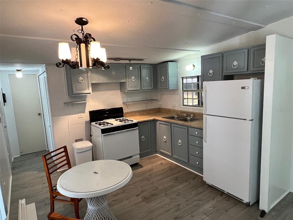 A kitchen features gray cabinets, white appliances, a small round table, and wood-look flooring — 11 SHADY LANE, PALMETTO, FL