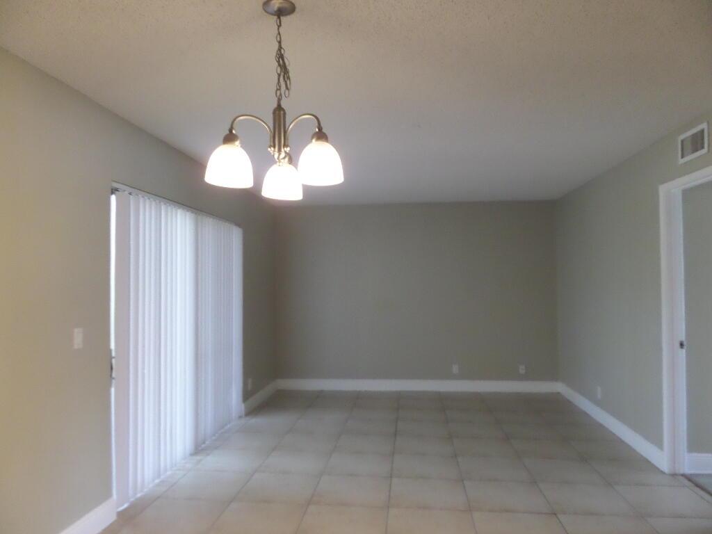 An empty dining room features tile flooring, a three-light chandelier, and vertical window blinds — 1440 Windorah Way # D, West Palm Beach FL 33411, WEST PALM BEACH, FL