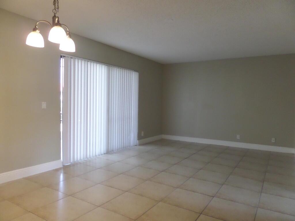 An empty room features light-colored tile flooring, beige walls, and a sliding glass door — 1440 Windorah Way # D, West Palm Beach FL 33411, WEST PALM BEACH, FL