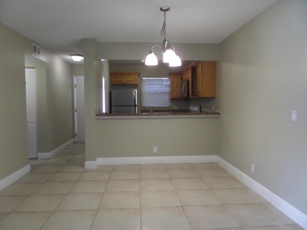 A dining area with tile flooring features a breakfast bar opening into a kitchen — 1440 Windorah Way # D, West Palm Beach FL 33411, WEST PALM BEACH, FL