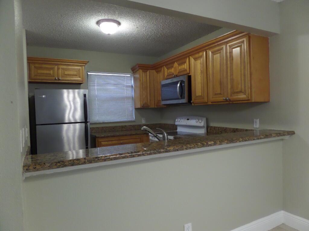 A kitchen with wood cabinets, stainless steel appliances, and a granite-topped breakfast bar — 1440 Windorah Way # D, West Palm Beach FL 33411, WEST PALM BEACH, FL