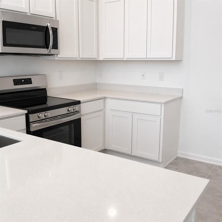 A kitchen features white cabinets, stainless steel appliances, and light-colored quartz countertops — 2528 SKYLINE LOOP, KISSIMMEE, FL